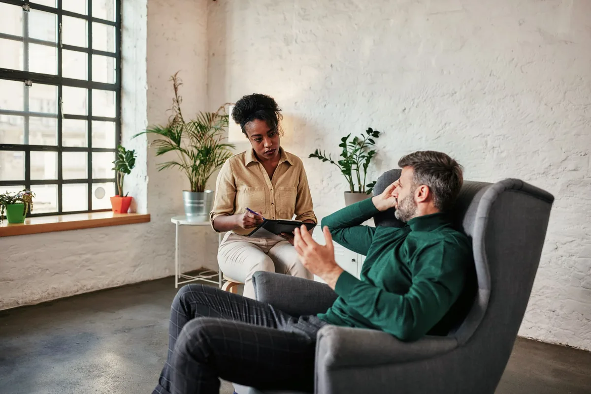 Counsellor listening and taking notes as a patient talks through his stress in a counselling session